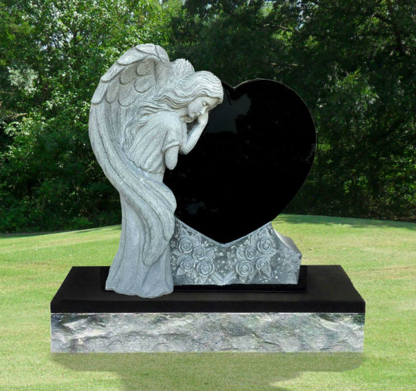 A graceful angel statue leans on a black heart-shaped monument, symbolizing love and remembrance, set against a serene green backdrop.